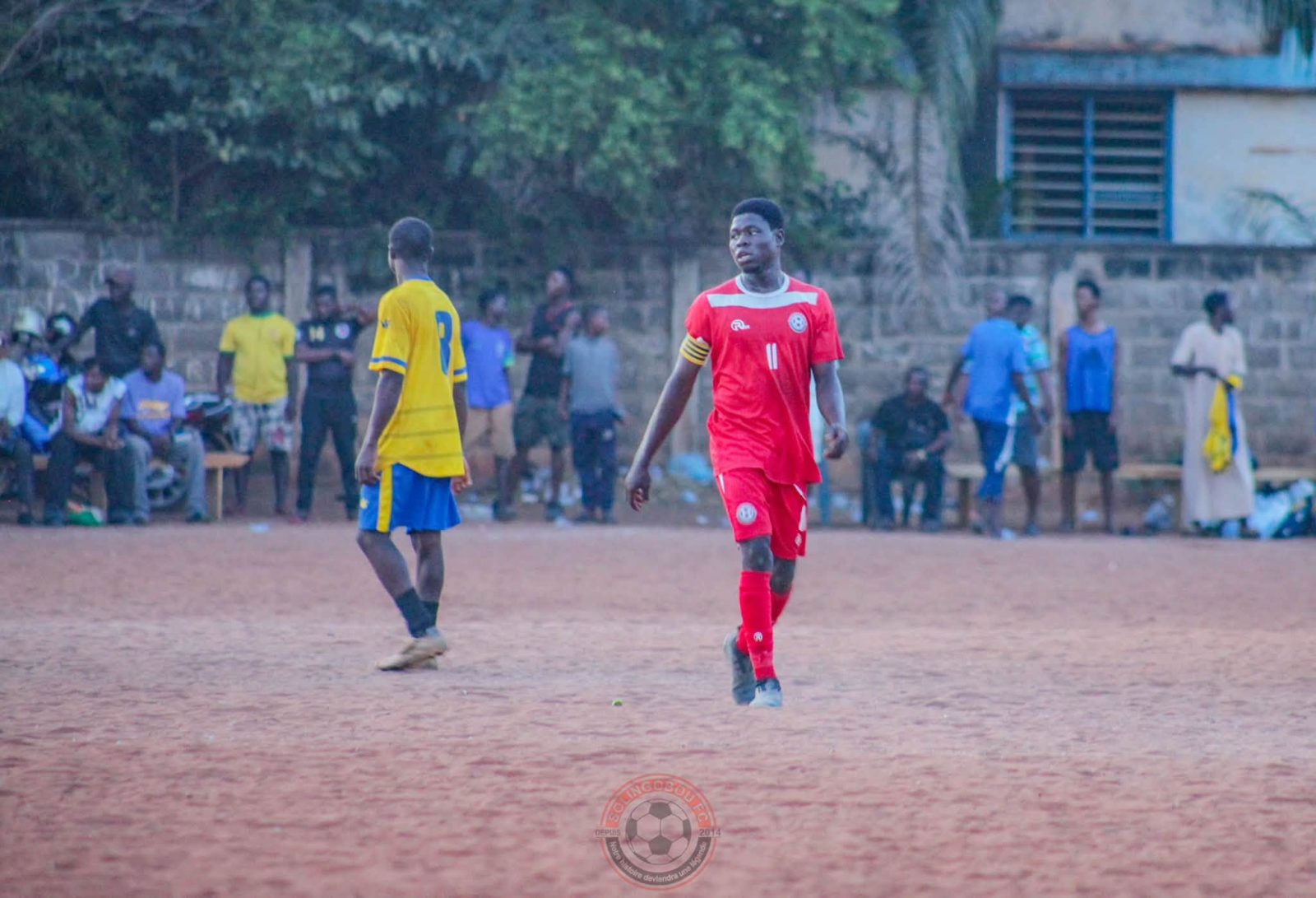 Match de Coupe du District sur un terrain en terre, devant le public